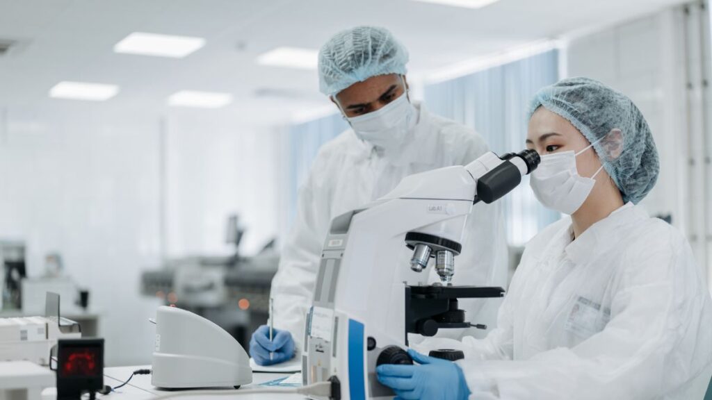 Medical researchers in protective gear working with a microscope in a cell cultivation facility (CPC).