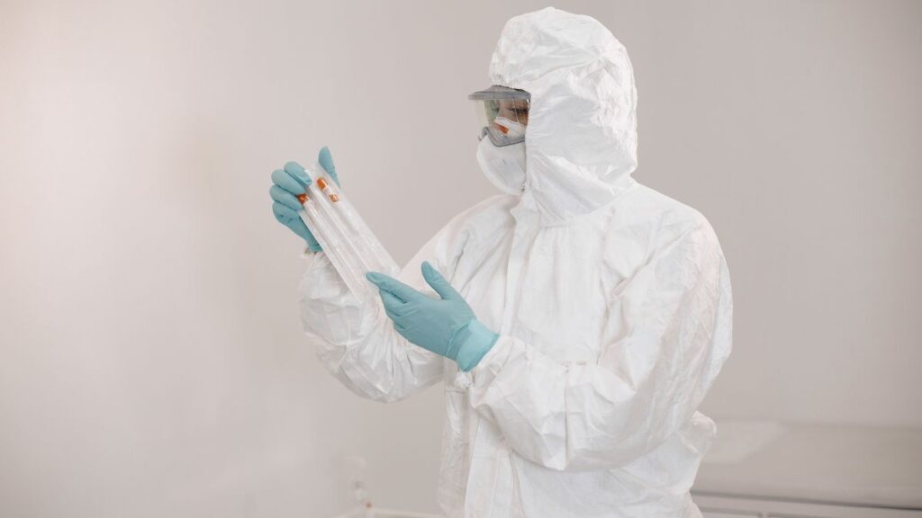 A technician in a full protective hazard suit examining test tubes in a laboratory.